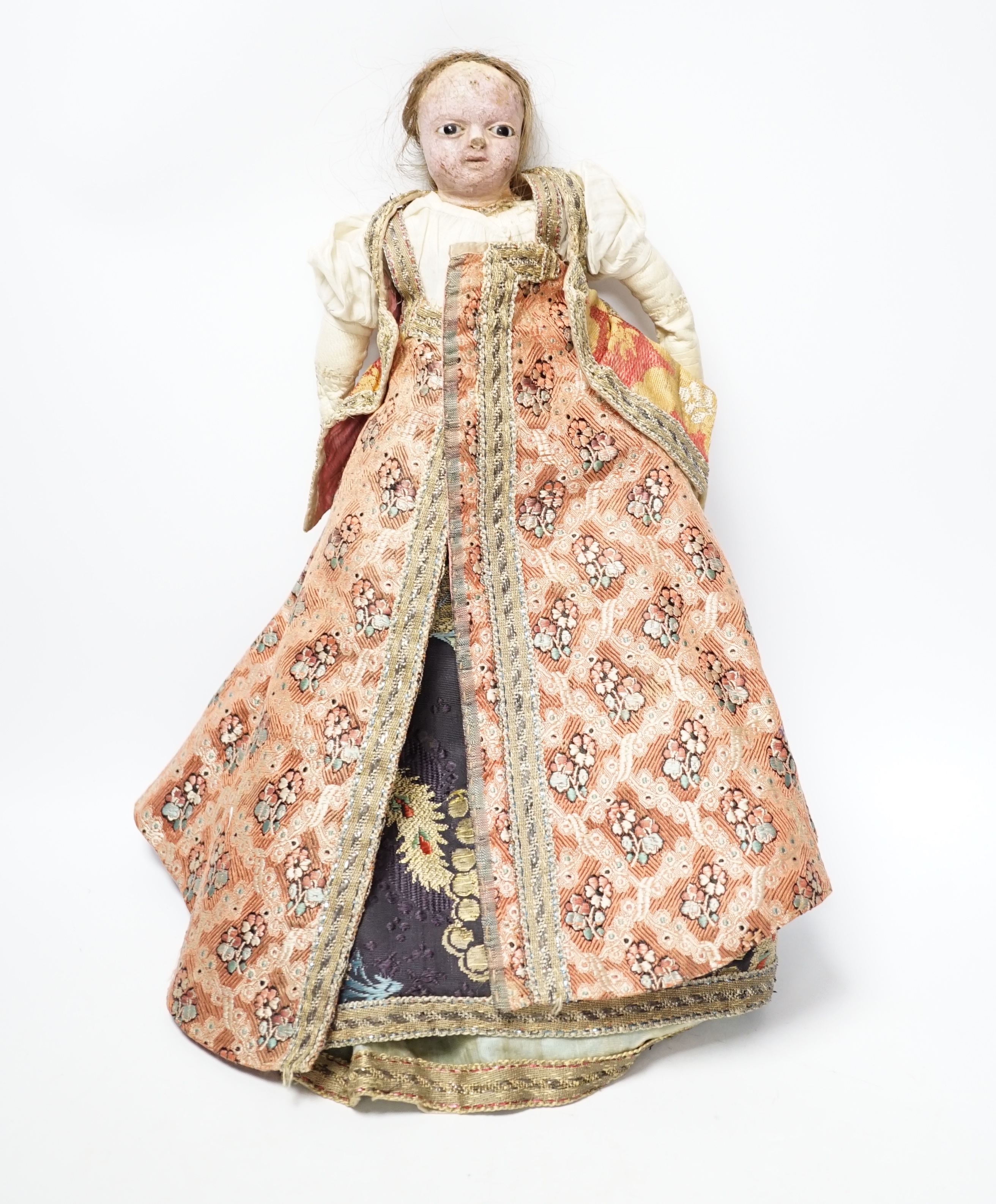 An early 19th century doll with a papier mache head, glass eyes and kid leather body, dressed in 18th century embroidered brocade and silk costume, possibly religious, 40cm high